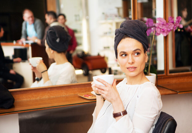 Female customer with towel around hair and coffee cup in hair salon